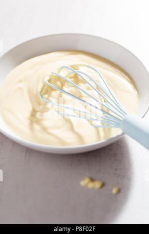 Ciotola di crema alla vaniglia con frusta blu Foto Stock