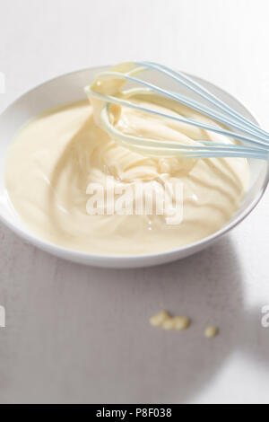 Ciotola di crema alla vaniglia con frusta blu Foto Stock