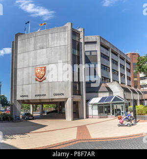 Vecchia donna in sella a una mobilità scooter passa la Civic Offices delle autorità locali, Woking Borough consiglio, Gloucester Square, Central Woking, Surrey, Regno Unito Foto Stock