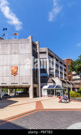 Vecchia donna in sella a una mobilità scooter passa la Civic Offices delle autorità locali, Woking Borough consiglio, Gloucester Square, Central Woking, Surrey, Regno Unito Foto Stock
