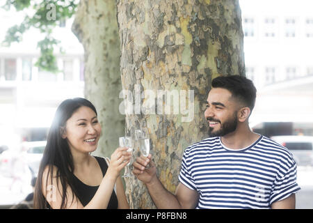 Giovane seduto sotto un albero a fare un brindisi celebrativo Foto Stock