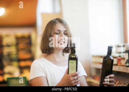 Donna in piedi in un supermercato confrontando le bottiglie di olio di oliva Foto Stock