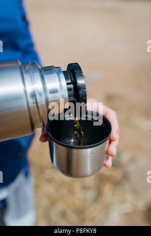 Donna versando il tè caldo da un thermos su di una spiaggia di sabbia in una giornata di sole. Close up. Foto Stock