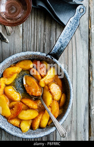 Pesche cotte in una padella su un sfondo di legno Foto Stock