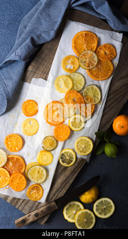 Arancia candita, limone e fettine di lime con un coltello su un tagliere di legno. Foto Stock