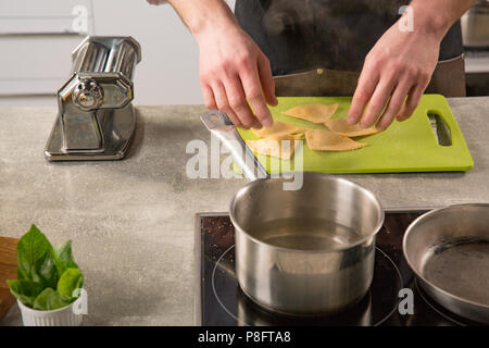 Un uomo mette le mani i ravioli in acqua bollente Foto Stock