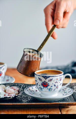 Una donna versando il caffè turco in un bagno turco di tazza di caffè da un rame caffè turco pot. Foto Stock