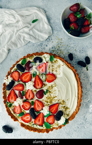 Fragola torta di formaggio photograhed su sfondo grigio dalla vista dall'alto. Una ciotola di frutti di bosco accompagna. Foto Stock