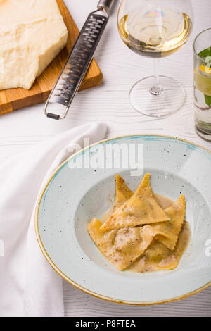 Ravioli italiani pasta sulla piastra con un pezzo di parmigiano e un bicchiere di vino bianco. foto verticale Foto Stock