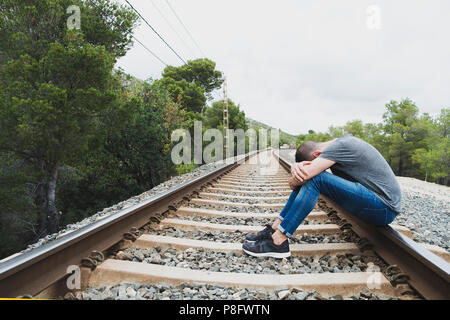 Un uomo caucasico, indossare abiti casual, avvolto a ricciolo sui binari della ferrovia, in un paesaggio naturale Foto Stock