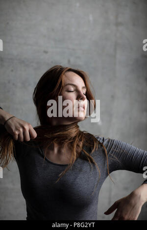 Modello femminile legatura di propri capelli intorno al suo collo mentre lo sguardo grazioso. Medium Shot. Foto Stock