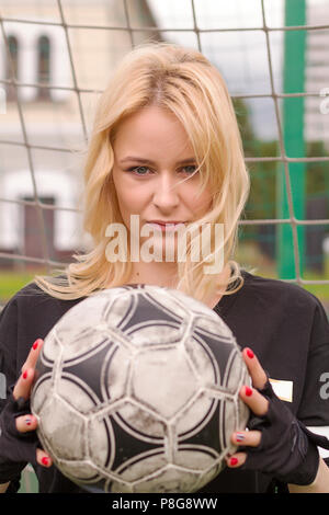 Bella bionda con una sfera all'obiettivo di calcio. Campo di calcio al cancello di close-up. Foto Stock