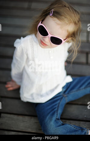 Adorabile bambina in occhiali da sole seduto su un pavimento di legno Foto Stock