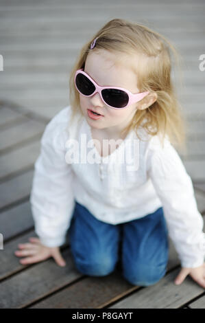 Adorabile bambina in occhiali da sole seduto su un pavimento di legno Foto Stock