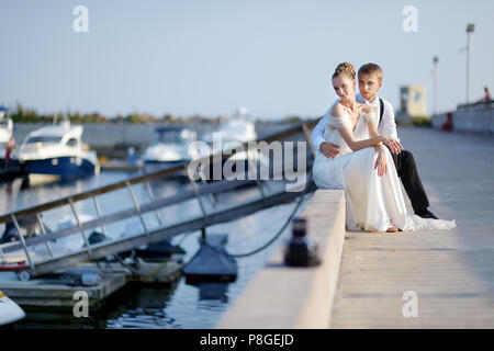Felice sposa e lo sposo seduta sul molo nel piccolo porto Foto Stock
