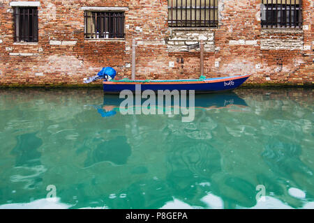 Barca blu nella parte anteriore della parete di piastrelle galleggiante sull'acqua verde smeraldo, Venezia Italia Foto Stock