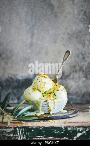 Ciotola di pistacchio casalinga gelato con pistacchio verde dadi sul legno rustico bancone cucina, muro di cemento a sfondo, copia dello spazio. Estate refre Foto Stock