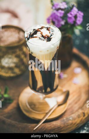 Iced mocha caffè con panna montata, gelato e salsa al cioccolato, servita nel bicchiere alto in legno sfondo a trama. In estate il concetto di bevande Foto Stock