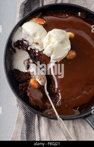 Brownie in una padella con un cucchiaio di gelato alla vaniglia e caramello salato e di arachidi tostate Foto Stock