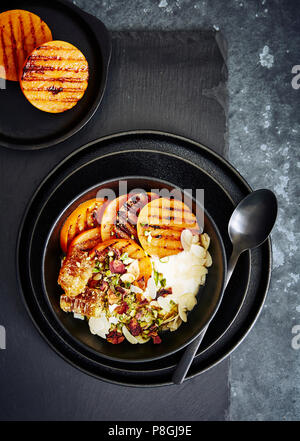 Grigliata di persimmon persiano con acqua di rose yogurt, dadi di mandorle e pistacchi, petali di rosa e miele pettine. Foto Stock