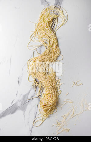 In casa italiana di pasta cruda spaghetti con farina di semola su marmo bianco sullo sfondo di texture. Appartamento laico, spazio. Foto Stock