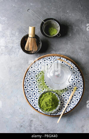 Ingredienti per fare matcha bere. Il tè verde Matcha in polvere in vaso di ceramica tradizionale cucchiaio di bambù e frusta sulla piastra decorativa, vetro teiera uovere Foto Stock