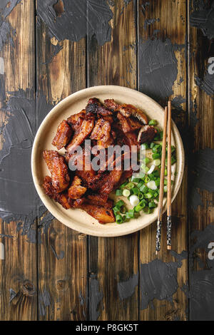 Cinese tradizionale piatto Cantonese BBQ pancetta di maiale con cipolline servita nella piastra in ceramica con bacchette su legno scuro dello sfondo plank. La piatta Foto Stock