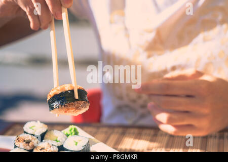 Donna con il Giappone bastoni mangia sushi in street cafe Foto Stock