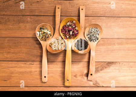 Cucchiai di legno con diverse erbe per infusione, in stile rustico, su sfondo di legno. Foto Stock