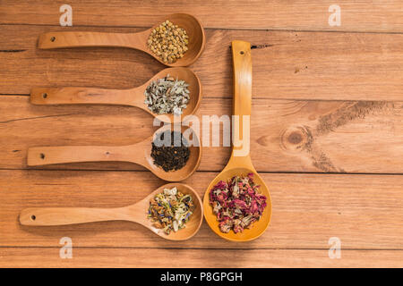 Cucchiai di legno con diverse erbe per infusione, in stile rustico, su sfondo di legno. Foto Stock