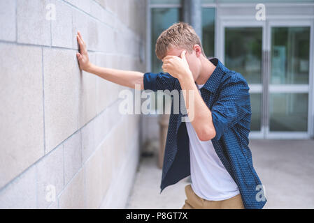 Sconvolto teen appoggiata contro un muro di mattoni al di fuori di un edificio pubblico. Foto Stock