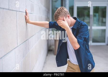 Sconvolto teen appoggiata contro un muro di mattoni al di fuori di un edificio pubblico. Foto Stock