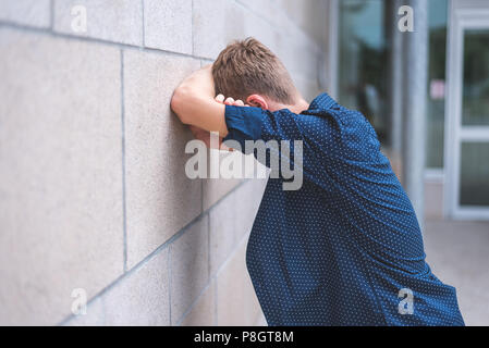 Teen gridando in bracci ripiegati contro un muro di mattoni. Foto Stock