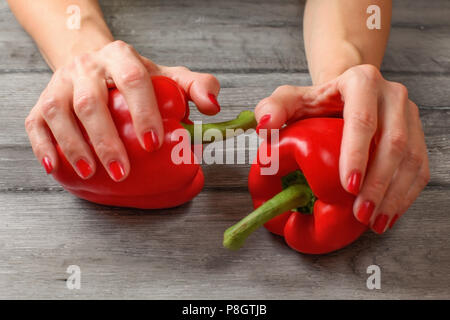 Donna mani due peperoni rossi collocati su grigio scrivania di legno. Foto Stock