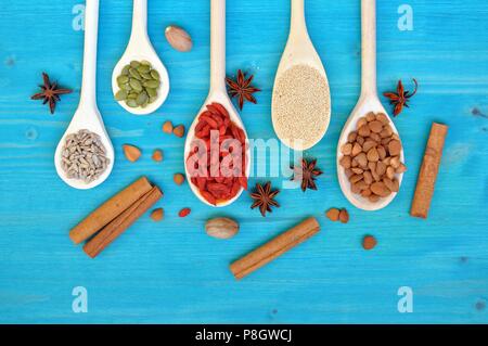 Concetto di tabella con colorate semi aromatiche e frutta in cucchiai di legno, su sfondo blu, piana, laici top table, spazio di copia Foto Stock