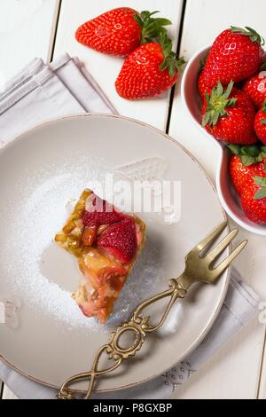 Direttamente sopra vista sulla metà mangiato pezzo di fragole e rabarbaro torta sulla tavola di legno tavolo e forcella in ottone Foto Stock