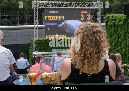 Londra, UK.11 Luglio, 2018. Il convogliatore, More London Place, Londra Centrale. Una giovane donna seduta con un fresco drink orologi Wimbledon Tennis Championships 2018 su uno schermo di grandi dimensioni come parte del 'Summer dal fiume' iniziativa come Roger Federer perde il suo quarto di finale contro Kevin Anderson e perde la possibilità di realizzare il suo sogno di vincere un altro grande slam campionato. Credito: Steve Hawkins Fotografia/Alamy Live News Foto Stock