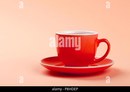 Chiudere uno rosso tazza di tè o caffè sul piattino pastello su carta rosa, sfondo basso angolo vista laterale Foto Stock