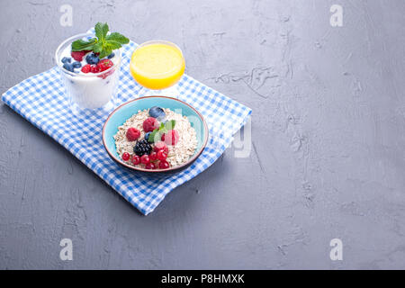 Delizioso e salutare prima colazione, sfondo grigio e igienico. Yogurt, muesli, granola, lampone e mirtillo bacche e succo d'arancia fresco. Spazio di copia Foto Stock