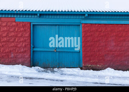 Il cancello di legno vecchio capannone, mattoni rossi con blue door, tetto e strada coperta in inverno la neve Foto Stock