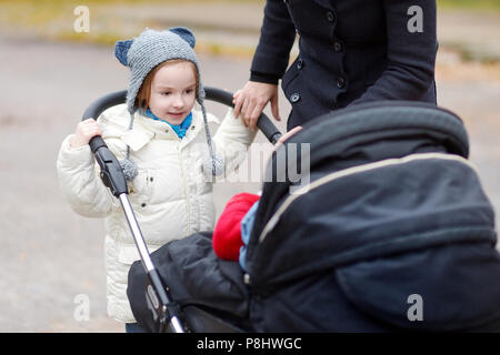 Piccola Sorella di spingere un passeggino con la sua piccola gemelli Foto Stock