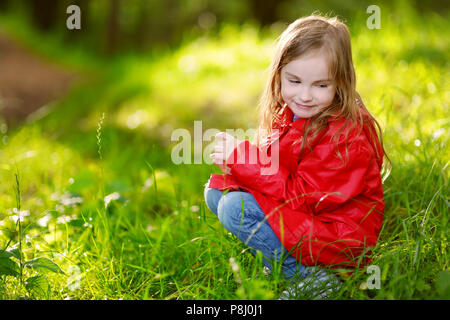 Adorabile bambina indossando giacca rossa seduta su un'erba sulla bellissima giornata autunnale Foto Stock