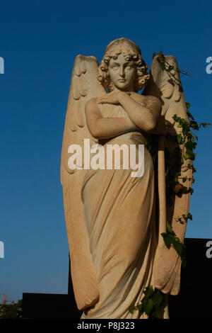 Una statua di una bella ragazza o angel nell'Addolorata cimitero, Malta, con un cielo blu chiaro dietro di lei Foto Stock