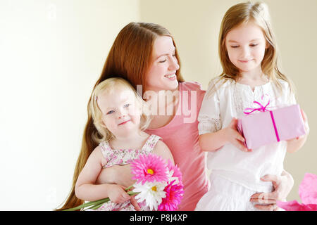 Giovane madre e la sua piccola figlie dando un regalo avvolto in rosa carta di avvolgimento e fiori Foto Stock