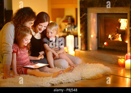 Felice famiglia giovane utilizzando un tablet pc a casa da un camino in un caldo e accogliente soggiorno sulla giornata invernale Foto Stock