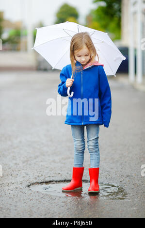 Adorabili poco ragazza con ombrello bianco in piedi in una pozza sul giorno di autunno caldo Foto Stock