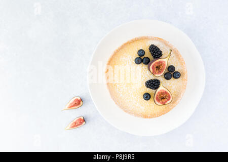 Vista dall'alto di una crostata al limone decorata con figure, mirtilli e more su fondo azzurro con copia spazio. Foto Stock