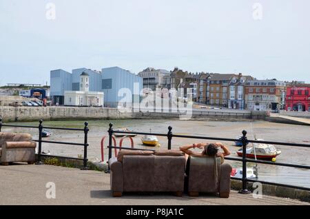 Uomo seduto sul divano che si affaccia margate dalla parete del porto Kent REGNO UNITO Foto Stock