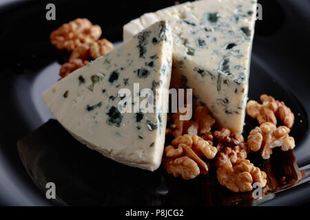 Cunei di soft formaggio blu con le noci su una piastra nera. Foto Stock