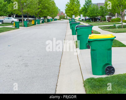 Fila di cassonetti allineati lungo la strada in un bel quartiere urbano in attesa di essere raccolti per lo smaltimento dei rifiuti Foto Stock